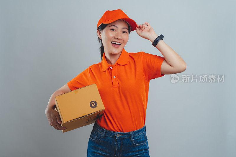 亚洲女人穿着统一的polo t恤，拿着盒子，开心兴奋地站在白色的背景上。